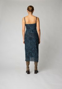 Rochie midi cu model albastru, cu bretele subțiri, textură transparentă și croială dreaptă, completată cu botine maro cu toc, până la genunchi.