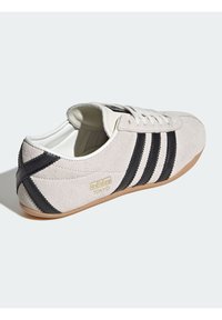 Gray suede shoe with black stripes, white leather accents, and a gum rubber sole. Features "adidas TOKYO" branding in gold.