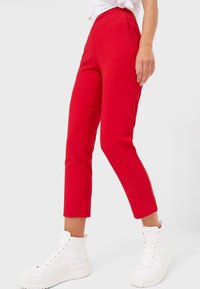 Red tailored pants with a slim fit, featuring a high waist, flat front, and cropped length, paired with white high-top sneakers.