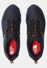 Paire de chaussures de trail The North Face bleu foncé avec des accents orange et des semelles intérieures rouges affichant le logo de la marque vues de dessus.
