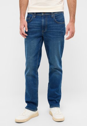 Blue denim jeans with a straight-leg cut, five-pocket design, contrasting stitching, and worn texture, paired with white sneakers.