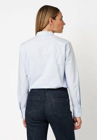 Light blue button-up shirt with a structured collar, long sleeves, and tailored fit, paired with dark denim jeans featuring back pockets.