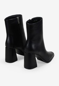 Botines de cuero negro con cierre de cremallera, tacones cuadrados y un diseño ajustado y elegante. Textura suave con punta afilada.