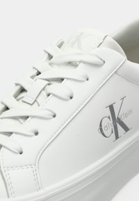 Witte lederen sneaker met een gladde textuur, ronde neus, platte veters en een zijlogo "CK". Minimalistisch ontwerp met subtiele merkdetails.