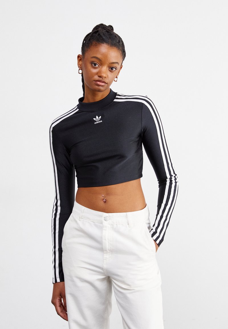 Top preto cropped de mangas longas com gola alta, apresentando um design de três riscas brancas nas mangas e um pequeno logo branco no peito.