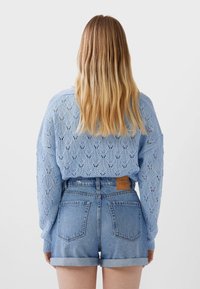 Světlomodrý pletený svetr s krajkovým vzorem, doplněný džínovými šortkami s nášivkou na pasu a ohrnutými lemy.