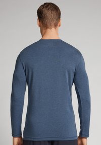 Tmavě modrá košile s dlouhými rukávy, vyrobená z měkkého materiálu, s klasickým kulatým výstřihem a přiléhavým střihem, který se směrem k pasu zužuje.