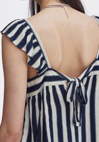 Haut rayé marine et crème avec manches à volants, dos ouvert et détail nœud papillon. Tissu léger avec finition texturée.