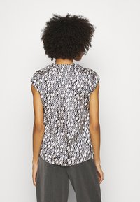 Bluzka z krótkim rękawem wykonana z lekkiego materiału, zdobiona geometrycznym wzorem w czerni i beżu. Zaokrąglony dół z lekko opuszczonymi ramionami.