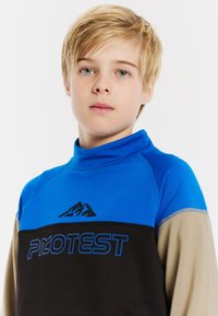 Modrá a čierna dlhá košeľa s vysokým golierom a grafikou hôr. Obsahuje kontrastné béžové rukávy a výrazný text "PROTEST".