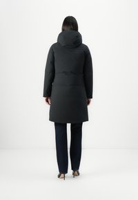 Zwarte geïsoleerde jas met een capuchon, middellange uitstraling, met een gladde textuur en een rechte snit. Gecombineerd met donkere denim broeken en hakken.