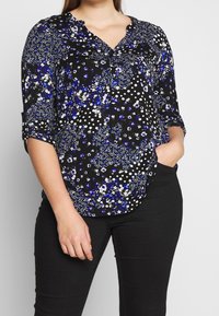 Svart blus med blommig och prickig mönster, med blå och vita accenter. V-halsdesign och uppkavlade ärmar. Mjuk tyg.