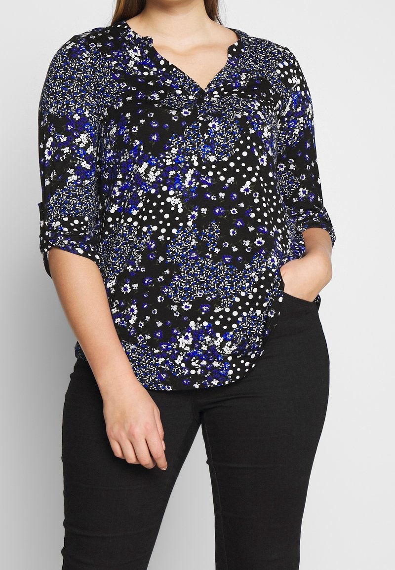 Svart blus med blommig och prickig mönster, med blå och vita accenter. V-halsdesign och uppkavlade ärmar. Mjuk tyg.