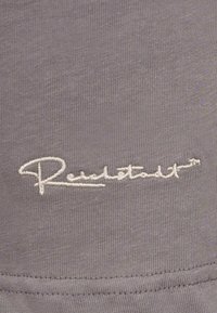 Tessuto grigio con una fine trama a righe presenta un ricamo della firma "Reichstadt" in bianco. Design semplice senza ulteriori motivi o accenti.