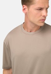 Krátký rukáv, tričko s kulatým výstřihem v světle béžové tkanině, které má hladkou strukturu a uvolněný střih s jemnými švy.