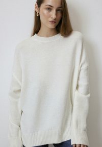 Cream-colored oversized sweater with a round neckline, ribbed cuffs, and hem. Soft texture, featuring dropped shoulders and relaxed fit.
