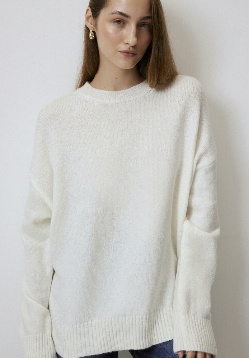 Cream-colored oversized sweater with a round neckline, ribbed cuffs, and hem. Soft texture, featuring dropped shoulders and relaxed fit.