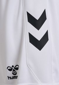 Witte sporttrui met zwarte chevronstrepen en een zwart logo met een bij-pictogram in de linkerbenedenhoek. Gestucte stof.