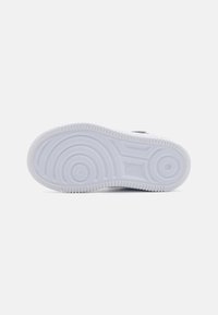 White rubber sneaker outsole featuring textured circular and wavy patterns, with a prominent brand logo embossed on the side.