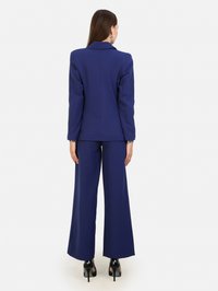 Granatowy garnitur z dopasowaną marynarką i szerokimi spodniami. Gładki materiał, długie rękawy oraz klasyczny krój klap. Szpilki dopełniają całość.
