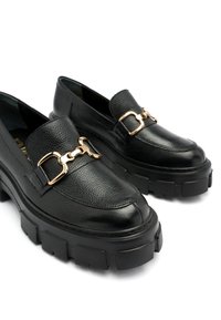 Czarne skórzane loafersy o teksturowanym wykończeniu, z akcentem w postaci złotej łańcuszkowej ozdoby oraz masywnymi czarnymi gumowymi podeszwami z bieżnikiem.