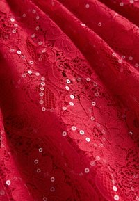 Czerwony koronkowy materiał z kwiatowymi wzorami i rozsypanymi cekinami, prezentujący teksturowaną powierzchnię z misternymi detalami.