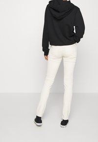 Sudadera negra con capucha, combinada con jeans blancos ajustados y zapatillas negras. Textura suave y diseño sencillo, costuras visibles en los pantalones.