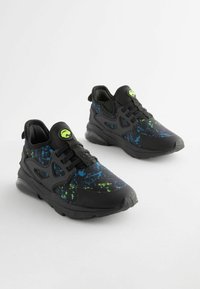 Black sneakers with a textured surface, featuring a colorful splatter pattern in blue and green. Includes a padded collar and lace-up design.