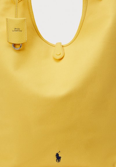 Żółta torba wykonana z fakturowanej tkaniny, o zaokrąglonym kształcie, z dodatkami ze skóry, metką z napisem "Polo by Ralph Lauren" oraz logo w kolorze granatowym.