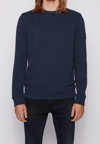 Sudadera azul marino en mezcla de algodón, con cuello redondo, mangas largas, puños de canalé y un sutil pespunte en V en el cuello.