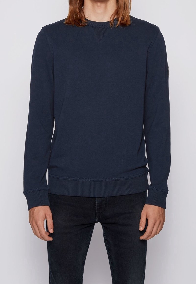 Sudadera azul marino en mezcla de algodón, con cuello redondo, mangas largas, puños de canalé y un sutil pespunte en V en el cuello.