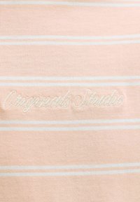 Ανοιχτό ροζ ύφασμα με λευκές οριζόντιες ρίγες και λευκό κεντητό κείμενο που λέει "Originals Studio" με καλλιγραφικά γράμματα.