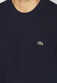 Marineblauer Rundhals-Pullover mit einem kleinen grünen Krokodil-Logo, das auf der linken Brust gestickt ist.