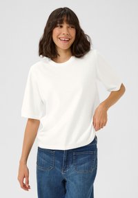 Pull court à manches courtes blanc avec col côtelé et texture douce, associé à un jean en denim bleu avec poches arrière.