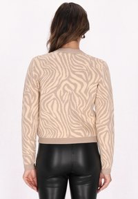 Beżowy sweter z teksturowanym wzorem zebra, z okrągłym dekoltem, długimi rękawami i ribbowanym wykończeniem, w połączeniu z czarnymi legginsami.