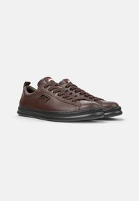 Baskets en cuir marron avec surface texturée, semelle en caoutchouc, bout rond, design à lacets et détails de marque minimalistes sur les côtés.