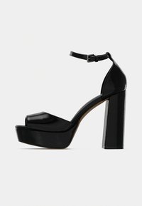 Μαύρα σανδάλια πλατφόρμας από λουστρίνι, με ανοιχτή μύτη, λουράκι στον αστράγαλο και χοντρό τακούνι. Λείο φινίρισμα και έντονο περίγραμμα.