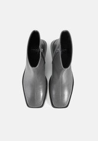 Stivali alla caviglia in pelle grigia con finitura liscia, punta quadrata e zip laterale, caratterizzati da una suola in gomma nera e un design minimalista.