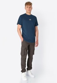 Marineblaues T-Shirt mit Rundhalsausschnitt und kurzen Ärmeln, kombiniert mit olivgrünen Cargo-Hosen mit mehreren Taschen und weißen Sneakers. Schlichtes Design.
