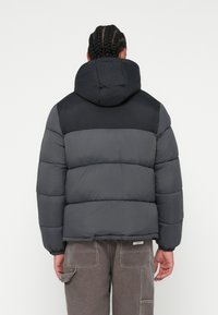 Puffer bunda v sivej farbe s čiernymi akcentmi, s kapucňou, prešívaným dizajnom a elastickými manžetami. Vyrobená z hladkého, ľahkého materiálu.