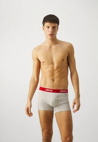 Szürke boxeralsó piros Levi's logós derékpánttal, testhez simuló kialakítással és puha pamut anyagból. A modell semleges arckifejezéssel áll.