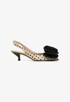 Beżowy but na niskim obcasie typu kitten heel ze skośnym paskiem, czarnymi groszkami i dużym czarnym kwiatem z materiału na spiczastym czubku.