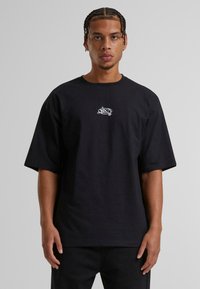 Sort t-shirt i bomuld med korte ærmer og en afslappet pasform. Har et hvidt grafisk logo på brystet. Enkel og uforfalsket design.