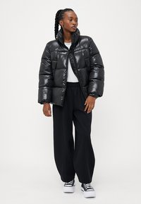 Sort pufferjakke med en blank overflade, der har høj krave og quiltet design. Sammen med løse sorte bukser og hvide sneakers.