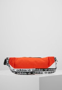 Orange waist bag made of durable fabric, featuring a black zipper and adjustable strap with white Adidas logo and pattern accents.
