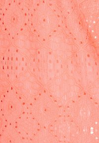 Tissu rose corail avec un motif en dentelle complexe présentant des formes losanges et de petits trous ouverts sur toute la surface.