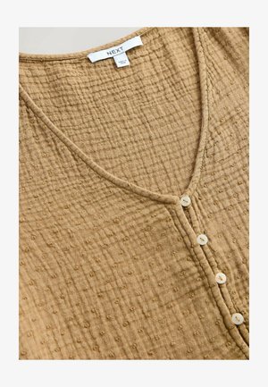 Tan, textured blouse with a V-neck and small buttons down the front. Features a soft, crinkled fabric with dot patterns throughout.