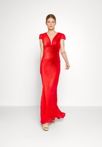Vestido de noite vermelho em renda, com um decote em V profundo e mangas curtas tipo cap sleeve, silhueta ajustada, e uma saia fluida que acentua o movimento.
