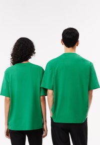 Grønne bomulds t-shirts med korte ærmer, løs pasform og rund hals. Begge har en ensfarvet og glat tekstur, vist fra ryggen.