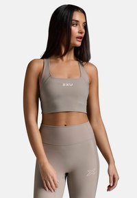 Svijetlosivi aktivni crop top s rebrastim naramenicama i suptilnim logotipom. Uparen s odgovarajućim tajicama visokog struka koje imaju rebrasti pojas.